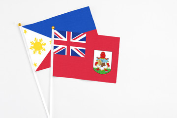 Fototapeta premium Bermuda and Philippines stick flags on white background. High quality fabric, miniature national flag. Peaceful global concept.White floor for copy space.