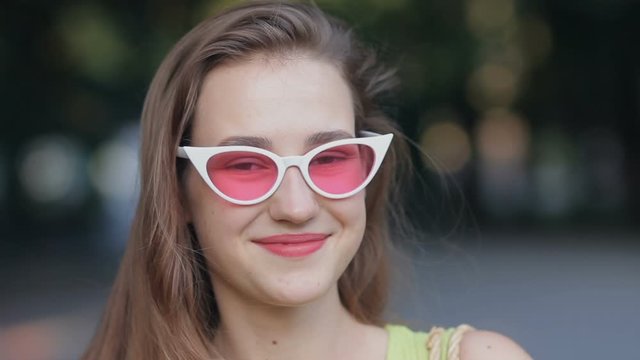 Pretty girl looking at camera and smiling wearing pink sunglasses