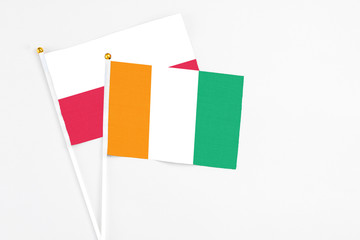 Cote D'Ivoire and Poland stick flags on white background. High quality fabric, miniature national flag. Peaceful global concept.White floor for copy space.