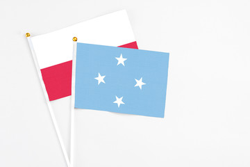 Micronesia and Poland stick flags on white background. High quality fabric, miniature national flag. Peaceful global concept.White floor for copy space.