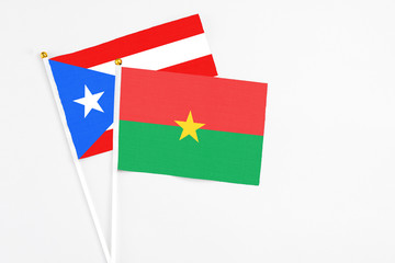 Burkina Faso and Puerto Rico stick flags on white background. High quality fabric, miniature national flag. Peaceful global concept.White floor for copy space.