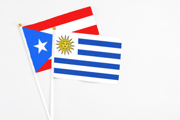 Uruguay and Puerto Rico stick flags on white background. High quality fabric, miniature national flag. Peaceful global concept.White floor for copy space.