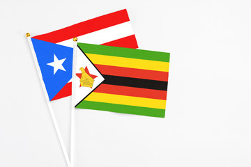 Zimbabwe and Puerto Rico stick flags on white background. High quality fabric, miniature national flag. Peaceful global concept.White floor for copy space.