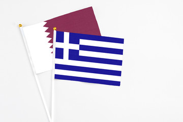 Greece and Qatar stick flags on white background. High quality fabric, miniature national flag. Peaceful global concept.White floor for copy space.