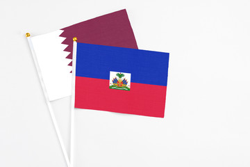Haiti and Qatar stick flags on white background. High quality fabric, miniature national flag. Peaceful global concept.White floor for copy space.