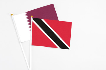 Trinidad And Tobago and Qatar stick flags on white background. High quality fabric, miniature national flag. Peaceful global concept.White floor for copy space.