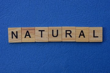 word natural made from brown wooden letters lies on a blue table