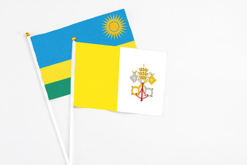 Vatican City and Rwanda stick flags on white background. High quality fabric, miniature national flag. Peaceful global concept.White floor for copy space.