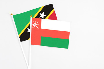 Oman and Saint Kitts And Nevis stick flags on white background. High quality fabric, miniature national flag. Peaceful global concept.White floor for copy space.