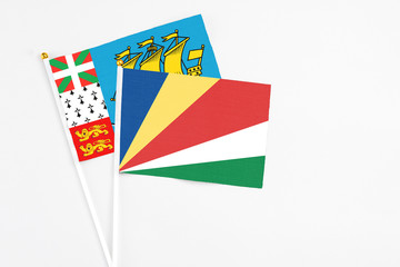 Seychelles and Saint Pierre And Miquelon stick flags on white background. High quality fabric, miniature national flag. Peaceful global concept.White floor for copy space.