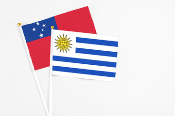 Uruguay and Samoa stick flags on white background. High quality fabric, miniature national flag. Peaceful global concept.White floor for copy space.