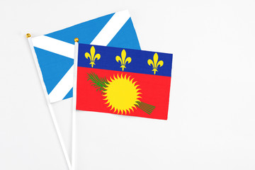 Guadeloupe and Scotland stick flags on white background. High quality fabric, miniature national flag. Peaceful global concept.White floor for copy space.