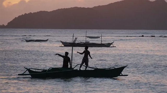 Silhouette of traditional filipino boat with two people moving around a beach near El Nido, Palawan, Philippines