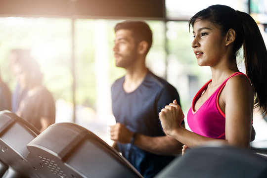 Asian fit beautiful female athlete in sportswear jogging on treadmill or running machine with Caucasian sport man in gym or fitness. Woman looking in front with smile and happy. Work out for health.