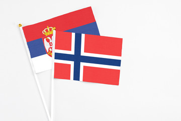 Norway and Serbia stick flags on white background. High quality fabric, miniature national flag. Peaceful global concept.White floor for copy space.