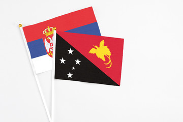 Papua New Guinea and Serbia stick flags on white background. High quality fabric, miniature national flag. Peaceful global concept.White floor for copy space.