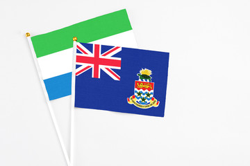 Fototapeta premium Cayman Islands and Sierra Leone stick flags on white background. High quality fabric, miniature national flag. Peaceful global concept.White floor for copy space.