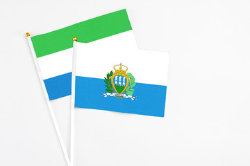 San Marino and Sierra Leone stick flags on white background. High quality fabric, miniature national flag. Peaceful global concept.White floor for copy space.