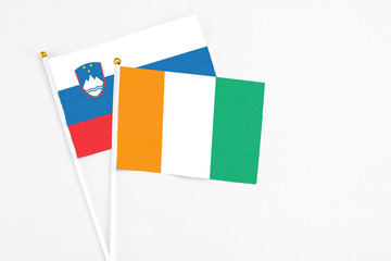 Fototapeta premium Cote D'Ivoire and Slovenia stick flags on white background. High quality fabric, miniature national flag. Peaceful global concept.White floor for copy space.