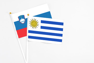 Uruguay and Slovenia stick flags on white background. High quality fabric, miniature national flag. Peaceful global concept.White floor for copy space.