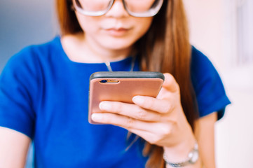 A young Asian woman in casual attire is using a smart phone indoor