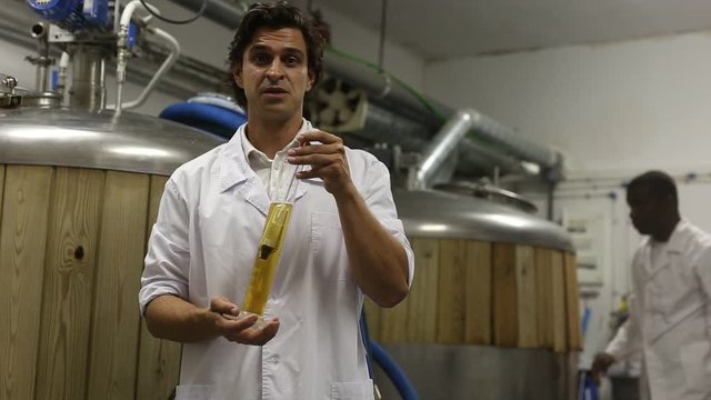 Two men experts is standing with flask of beer and analizying it in beer factory