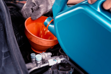 Car maintenance concept.Car mechanic replacing and pouring fresh oil into engine at maintenance...