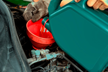 Car maintenance concept.Car mechanic replacing and pouring fresh oil into engine at maintenance...