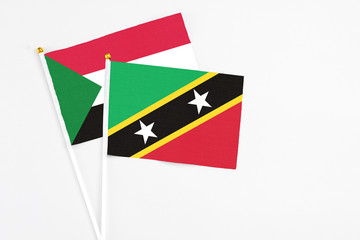 Saint Kitts And Nevis and Sudan stick flags on white background. High quality fabric, miniature national flag. Peaceful global concept.White floor for copy space.