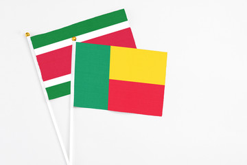 Benin and Suriname stick flags on white background. High quality fabric, miniature national flag. Peaceful global concept.White floor for copy space.
