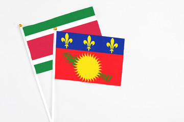 Fototapeta premium Guadeloupe and Suriname stick flags on white background. High quality fabric, miniature national flag. Peaceful global concept.White floor for copy space.