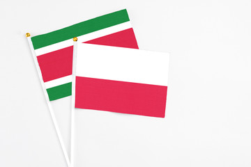Poland and Suriname stick flags on white background. High quality fabric, miniature national flag. Peaceful global concept.White floor for copy space.
