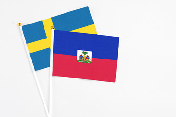 Haiti and Sweden stick flags on white background. High quality fabric, miniature national flag. Peaceful global concept.White floor for copy space.