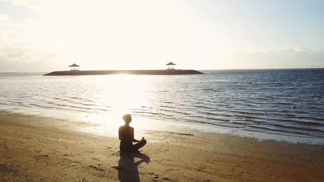 Silhouette of young woman meditating on beach