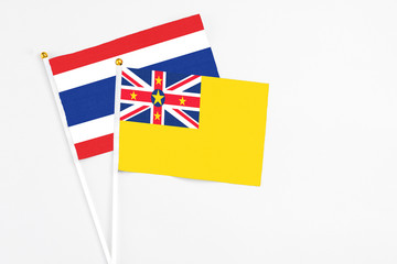Fototapeta premium Niue and Thailand stick flags on white background. High quality fabric, miniature national flag. Peaceful global concept.White floor for copy space.