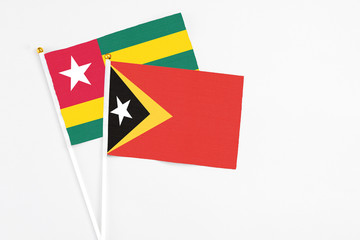 East Timor and Togo stick flags on white background. High quality fabric, miniature national flag. Peaceful global concept.White floor for copy space.