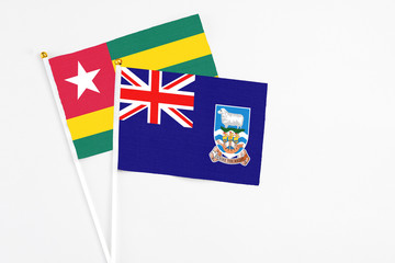 Fototapeta premium Falkland Islands and Togo stick flags on white background. High quality fabric, miniature national flag. Peaceful global concept.White floor for copy space.