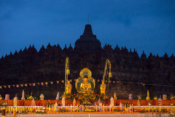 Fototapeta premium Golden Waisak (Vesak) altar in front of Borobudur Temple silhouette and deep blue dusk sky, an annual celebration of Gautama Buddha's birth, enlightenment and death, Java, Indonesia