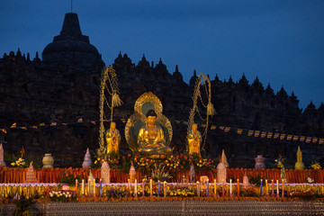 Golden Waisak (Vesak) altar in front of Borobudur Temple silhouette and deep blue dusk sky, an annual celebration of Gautama Buddha's birth, enlightenment and death, Java, Indonesia