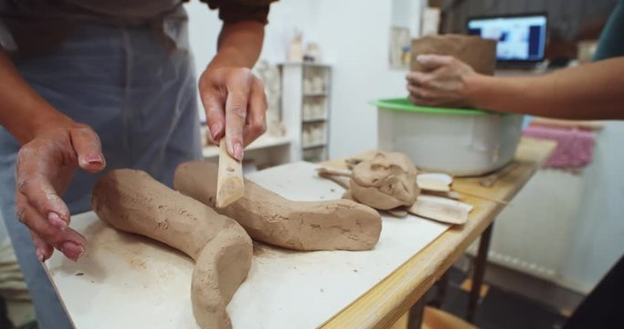 Close up of female hands performing clay form on pottery table with instruments. Handmade art object. Successful freelance educating lifestyle. Creative classroom for craft training. Adult educating.