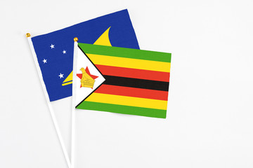 Zimbabwe and Tokelau stick flags on white background. High quality fabric, miniature national flag. Peaceful global concept.White floor for copy space.