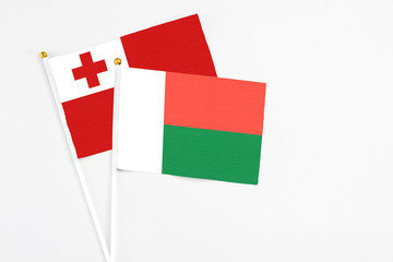 Fototapeta premium Madagascar and Tonga stick flags on white background. High quality fabric, miniature national flag. Peaceful global concept.White floor for copy space.