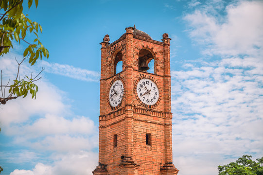 Clock tower built of brick, in the background a blue sky and some green trees