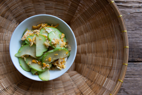 Fresh chayote fruits (Sechium edulis) stir fried with egg and garlic in bowl on wood background