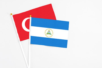 Nicaragua and Turkey stick flags on white background. High quality fabric, miniature national flag. Peaceful global concept.White floor for copy space.