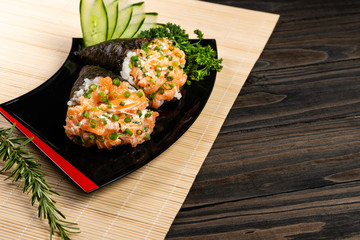 Salmon temaki sushi on black plate in black background.