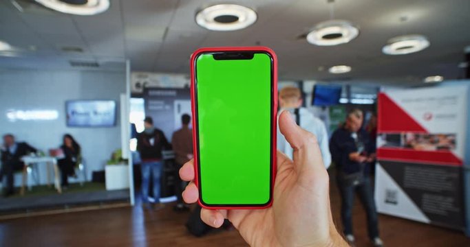 Closeup of man hand tapping green screen smartphone in modern meeting conference hall with business people on background. Partnership community. Education event for students. Certification training.