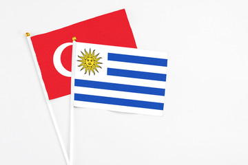 Uruguay and Turkey stick flags on white background. High quality fabric, miniature national flag. Peaceful global concept.White floor for copy space.