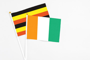 Fototapeta premium Cote D'Ivoire and Uganda stick flags on white background. High quality fabric, miniature national flag. Peaceful global concept.White floor for copy space.
