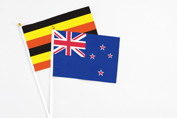 Fototapeta premium New Zealand and Uganda stick flags on white background. High quality fabric, miniature national flag. Peaceful global concept.White floor for copy space.